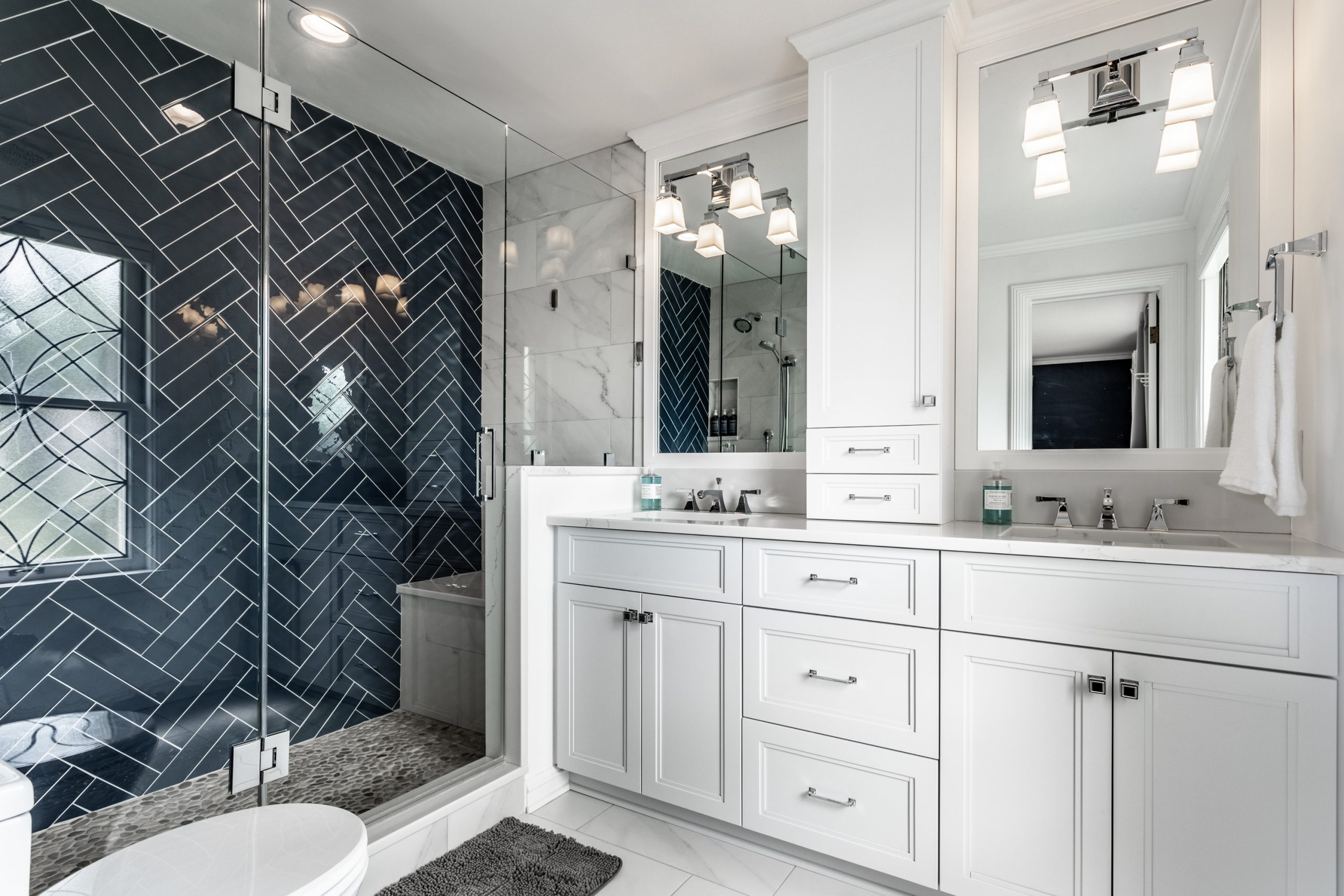newly renovated bathroom with walk-in shower with dark herringbone tiles and a double sink vanity