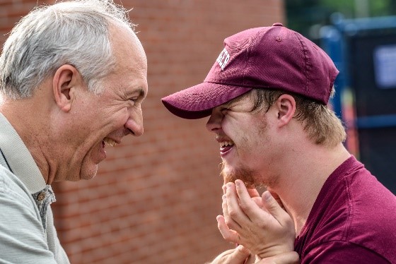 An older man and a younger man facing each other and smiling.