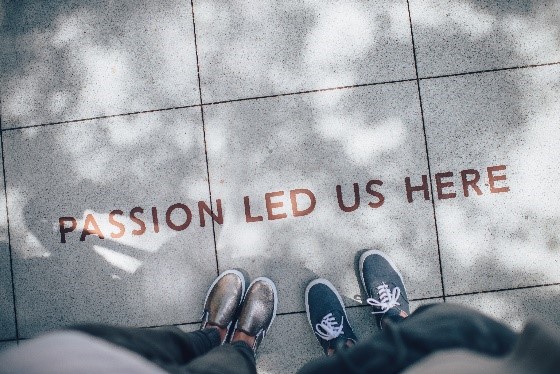 A sidewalk that has written on it, "PASSION LED US HERE" as two people stand looking down at it and their feet.